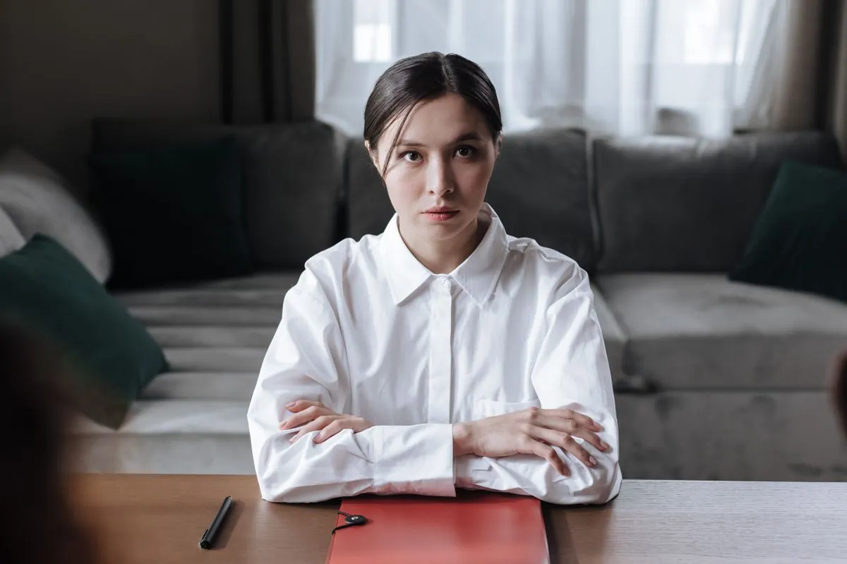 A serious-looking woman with folded arms, sitting at a table