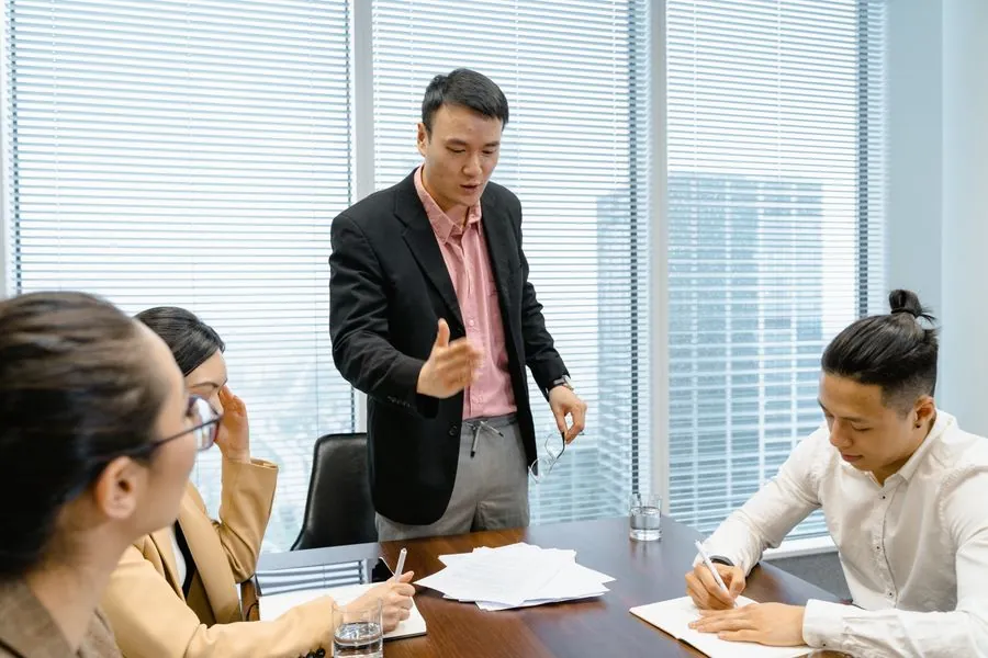 A manager talking to a colleague sitting at a desk in the office