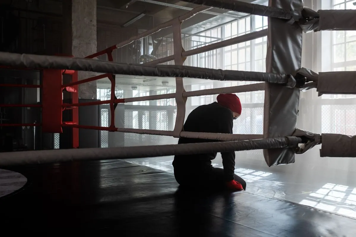 Güneş ışığı vuran boş bir spor salonunda, boks ringinde tek başına oturan bir boksör